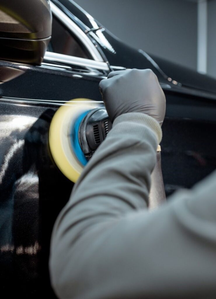 Professional detailer performing paint correction with a Rupes LHR 21 Mark III polisher on a black car in a detailing studio
